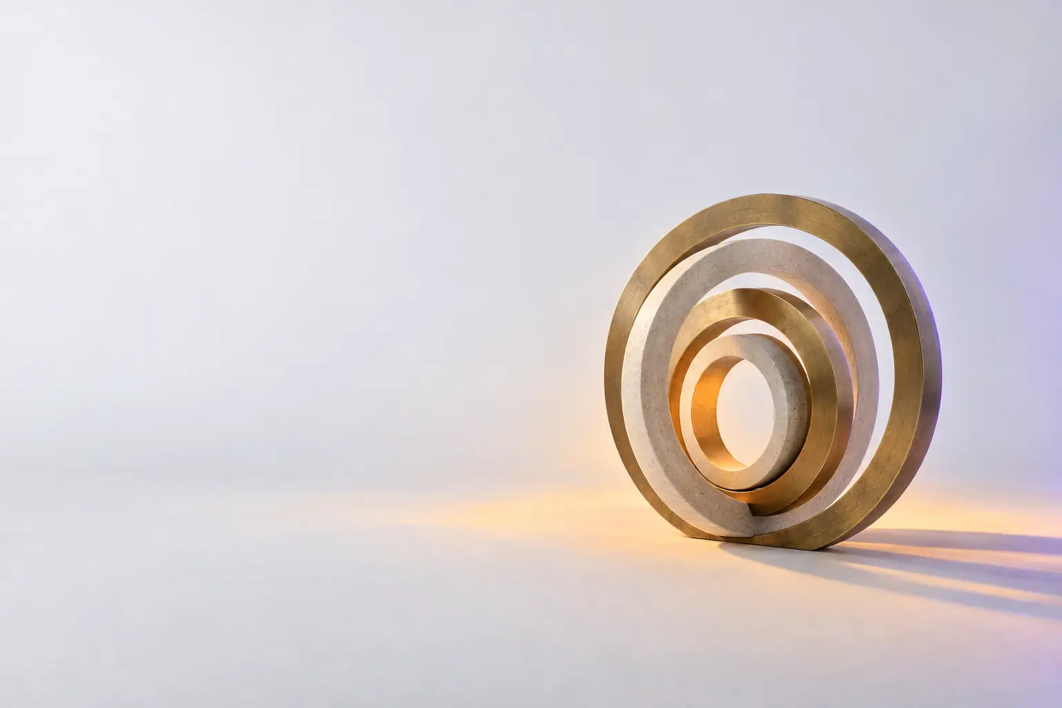 Five concentric rings of brass and pale stone nested like a camera aperture, the innermost ring lit warmly and the outer rings falling into shadow.