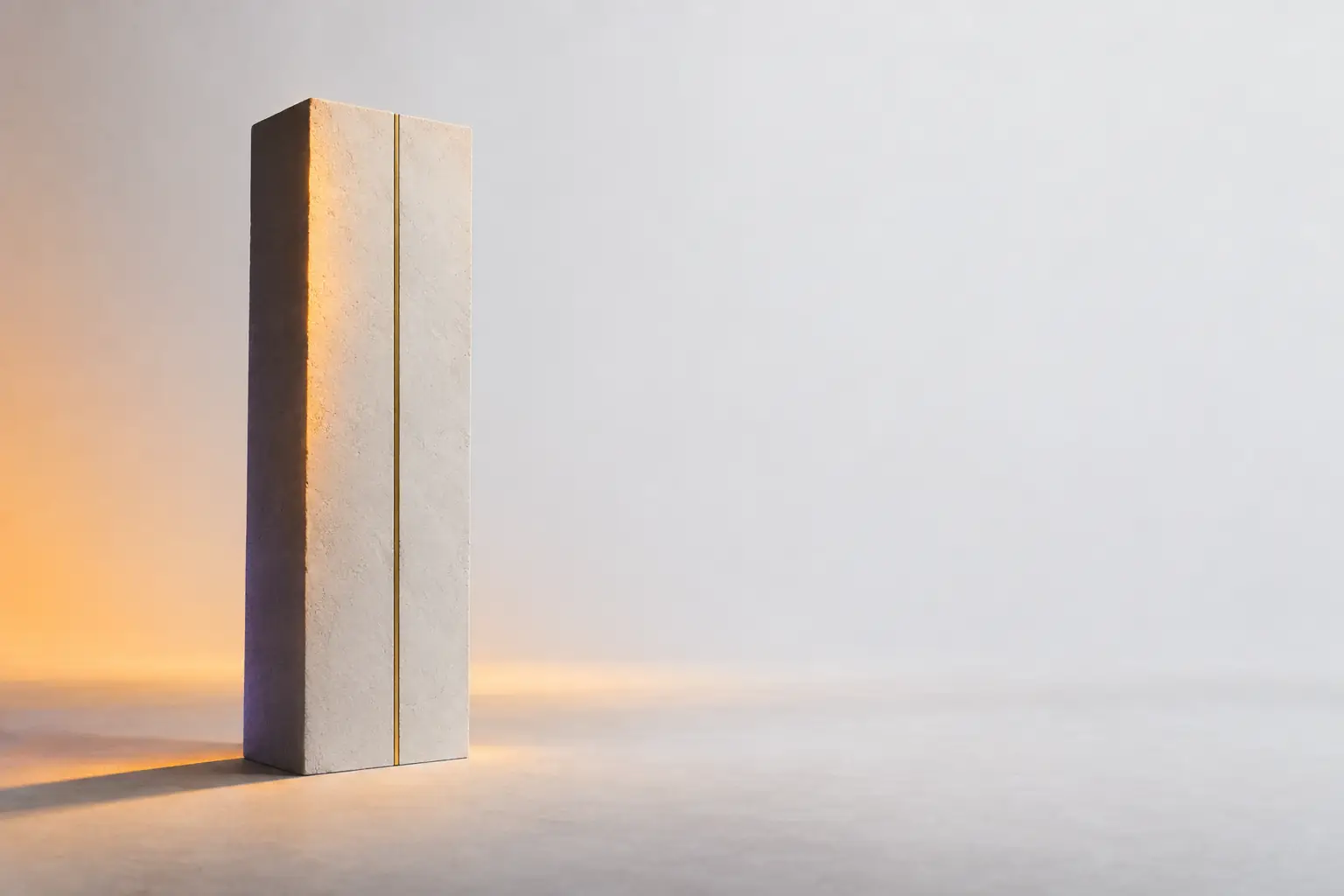 A tall matte plaster monolith standing alone, a single thin brass line inlaid down its lit face and the opposite face falling into deep shadow.